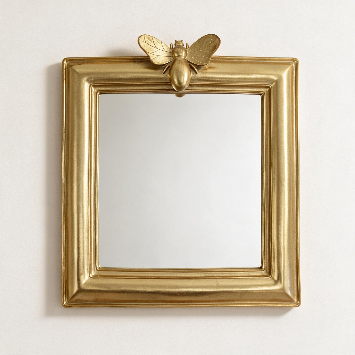 Lumara Bee Mirror in gold resin, square frame with bee motif, front view on warm white studio wall