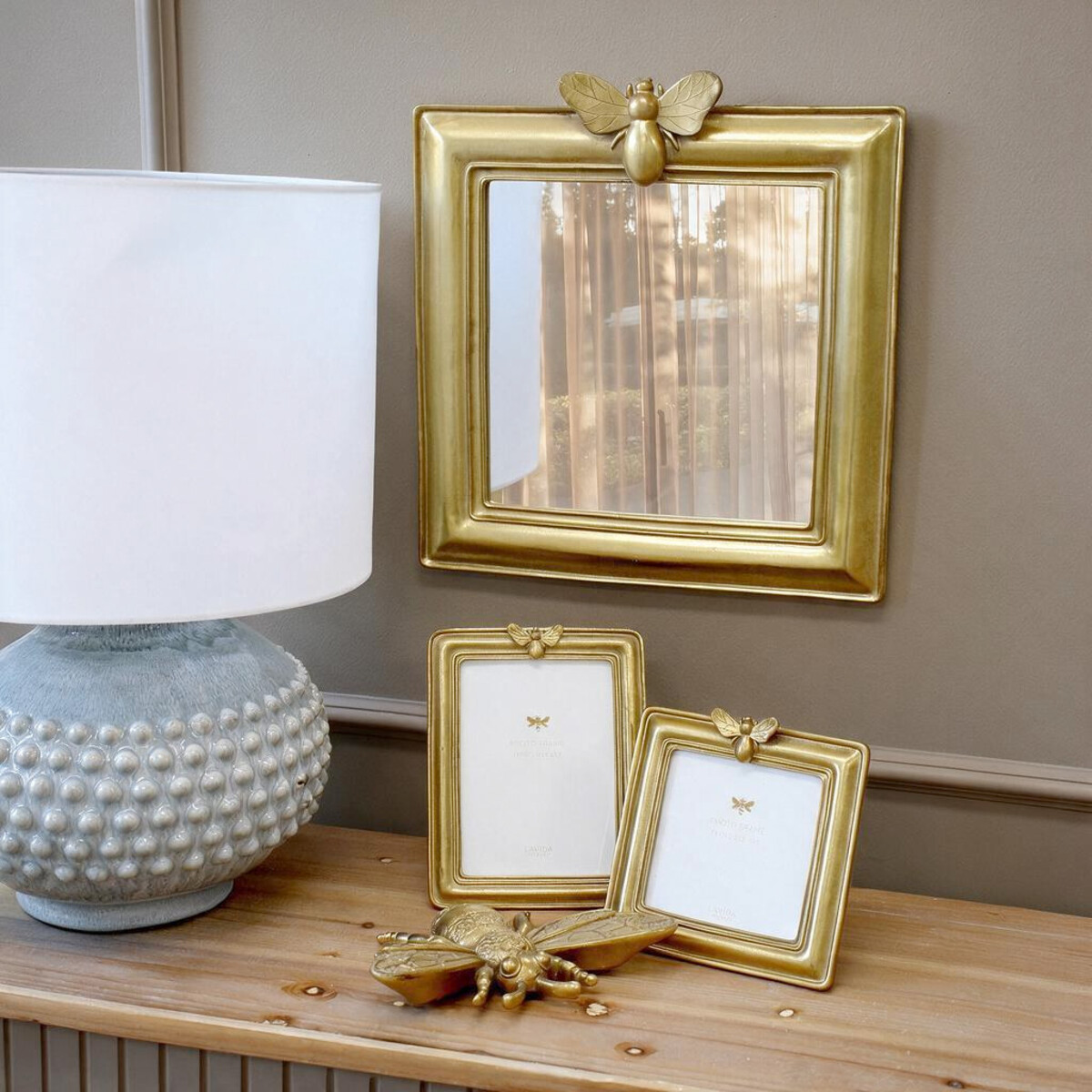 Lumara Bee Mirror at true scale above a timber console with table lamp and matching bee photo frames
