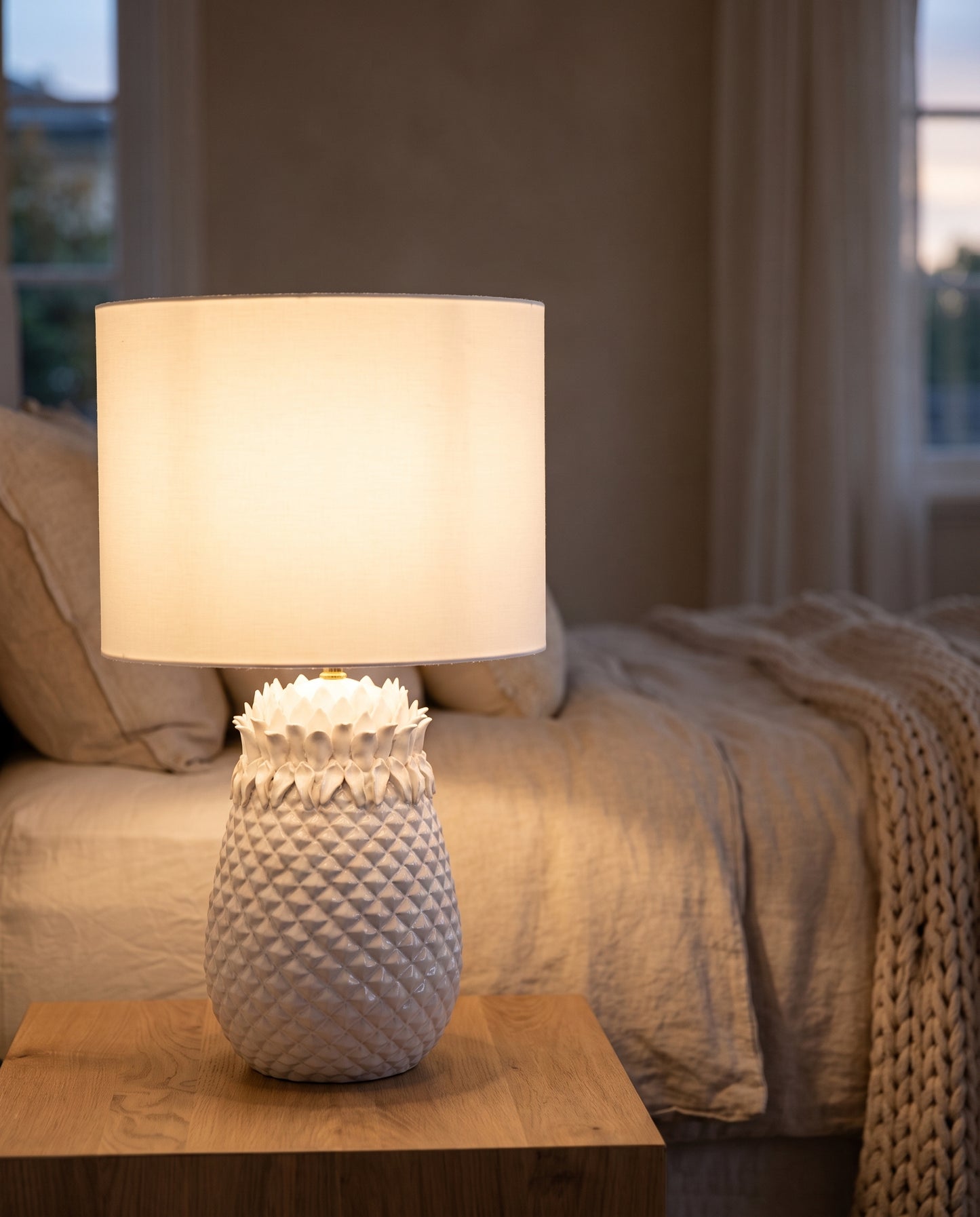 White Pineapple Table Lamp lit at dusk on a bedside table — Lumara Home